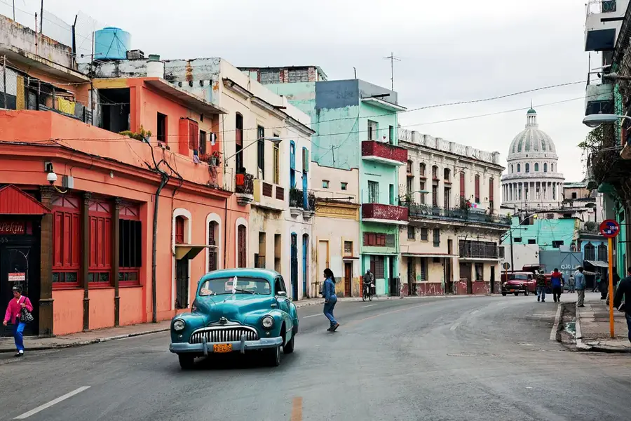 A lived-in Havana street with a classic car and the Capitolio beyond